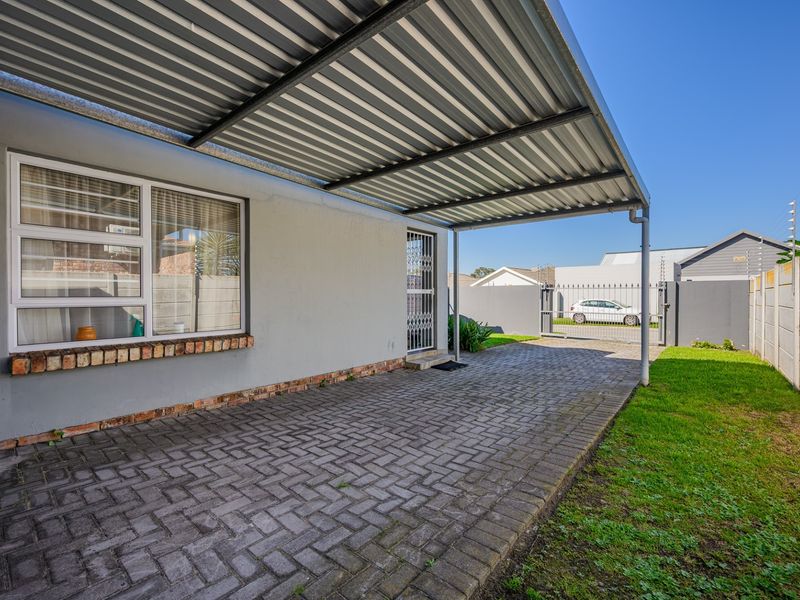 A covered outdoor patio area featuring paved flooring, a corrugated metal roof, and direct access to the property's driveway and garden.