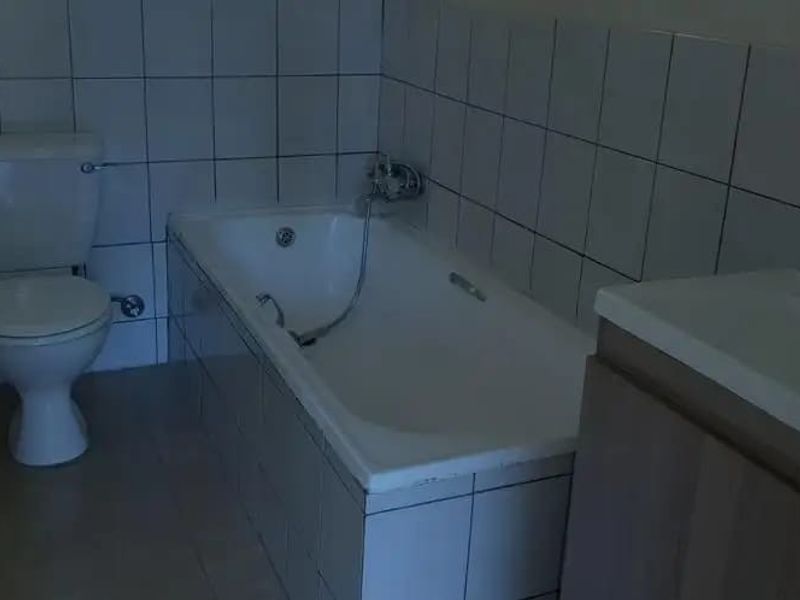 A functional bathroom featuring a standard bathtub with handheld shower mixer, a toilet, and a vanity cabinet with a built-in washbasin.