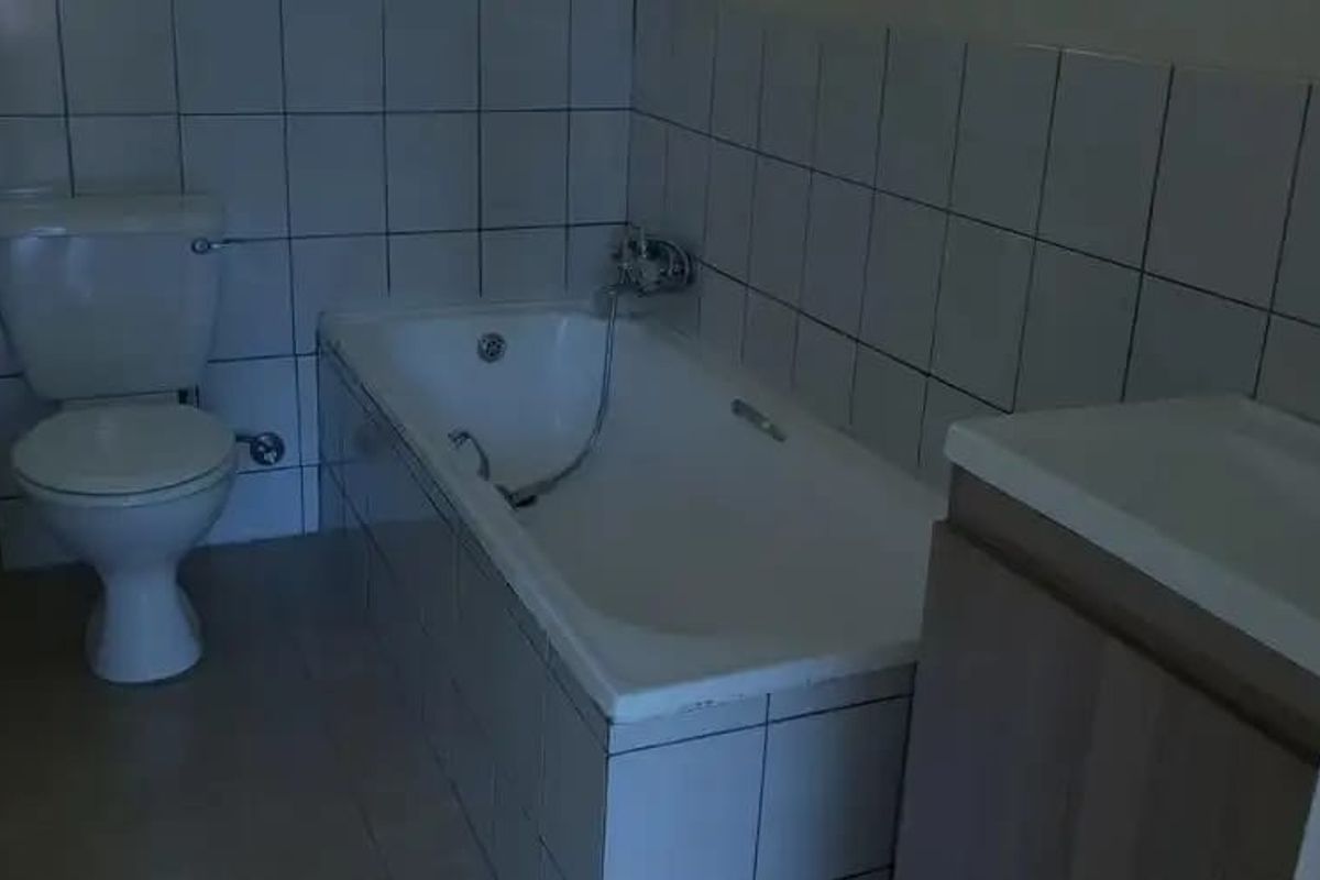 A functional bathroom featuring a standard bathtub with handheld shower mixer, a toilet, and a vanity cabinet with a built-in washbasin.