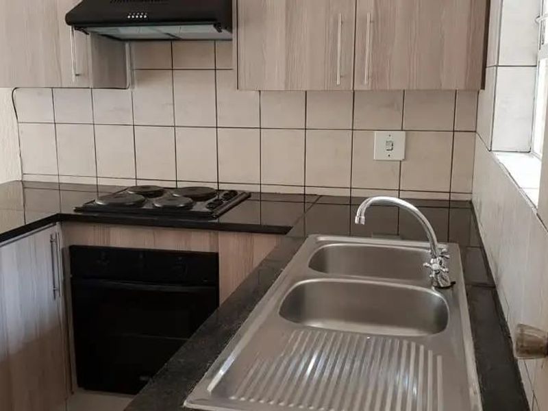 A clean, functional kitchen featuring built-in cabinetry, dark laminate countertops, a double stainless steel sink, and integrated electric cooking appliances with a tiled splashback.