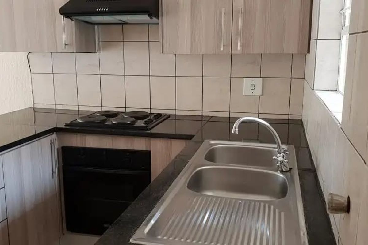 A clean, functional kitchen featuring built-in cabinetry, dark laminate countertops, a double stainless steel sink, and integrated electric cooking appliances with a tiled splashback.