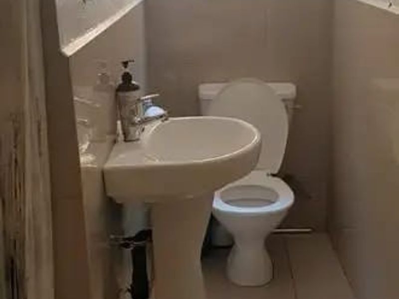 A compact bathroom featuring a pedestal basin, toilet, and tiled finishes, with a window providing natural light.
