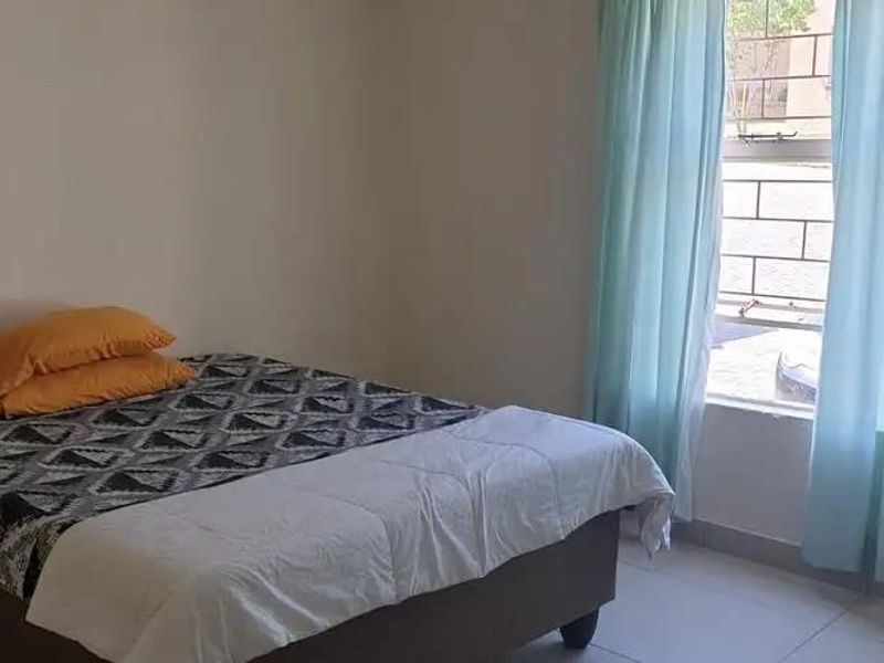 A simple bedroom featuring tiled flooring and a window fitted with security bars, providing natural light.