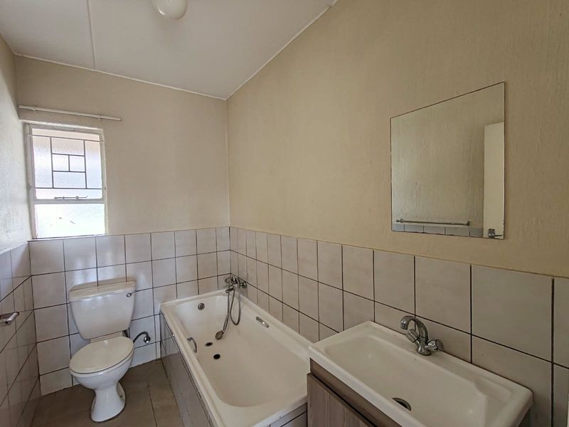 A functional bathroom featuring a bathtub, toilet, and vanity basin with a wall-mounted mirror and tiled splashback.