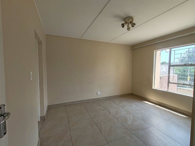 A clean, empty bedroom featuring neutral wall paint, tiled flooring, and a window with security bars, providing a blank canvas for personalization.