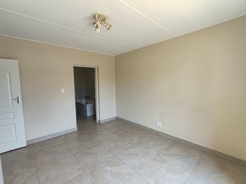 A spacious, empty bedroom featuring neutral wall tones, tiled flooring, and direct access to an adjoining bathroom.