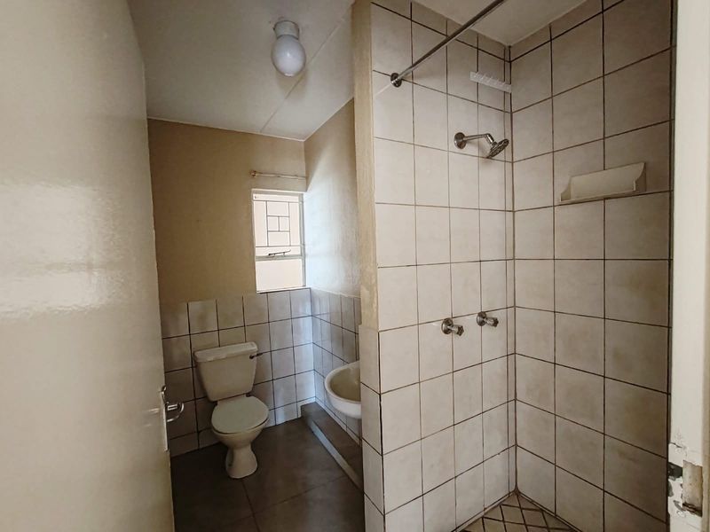 A functional bathroom featuring a shower, toilet, and wash basin with neutral wall and floor tiling, requiring cosmetic updates to improve its overall condition.
