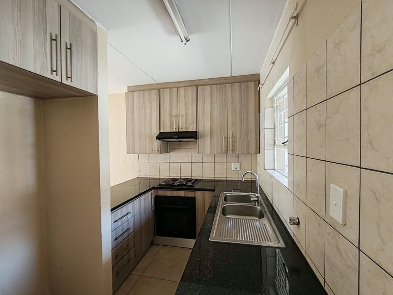 A functional kitchen featuring wood-finish cabinetry, granite countertops, a built-in oven and hob, and a stainless steel double sink with tiled backsplash.