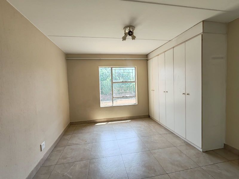 A vacant bedroom featuring tiled flooring, built-in cupboards, and a window with security bars, offering a neutral canvas for personalization.