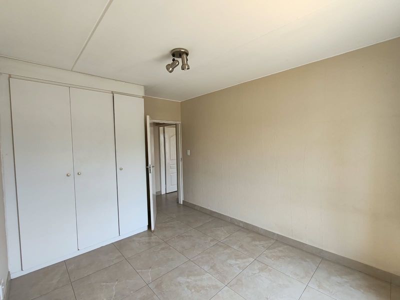 A clean, empty bedroom featuring neutral tiled flooring and built-in cupboards, offering a blank canvas for personalization.