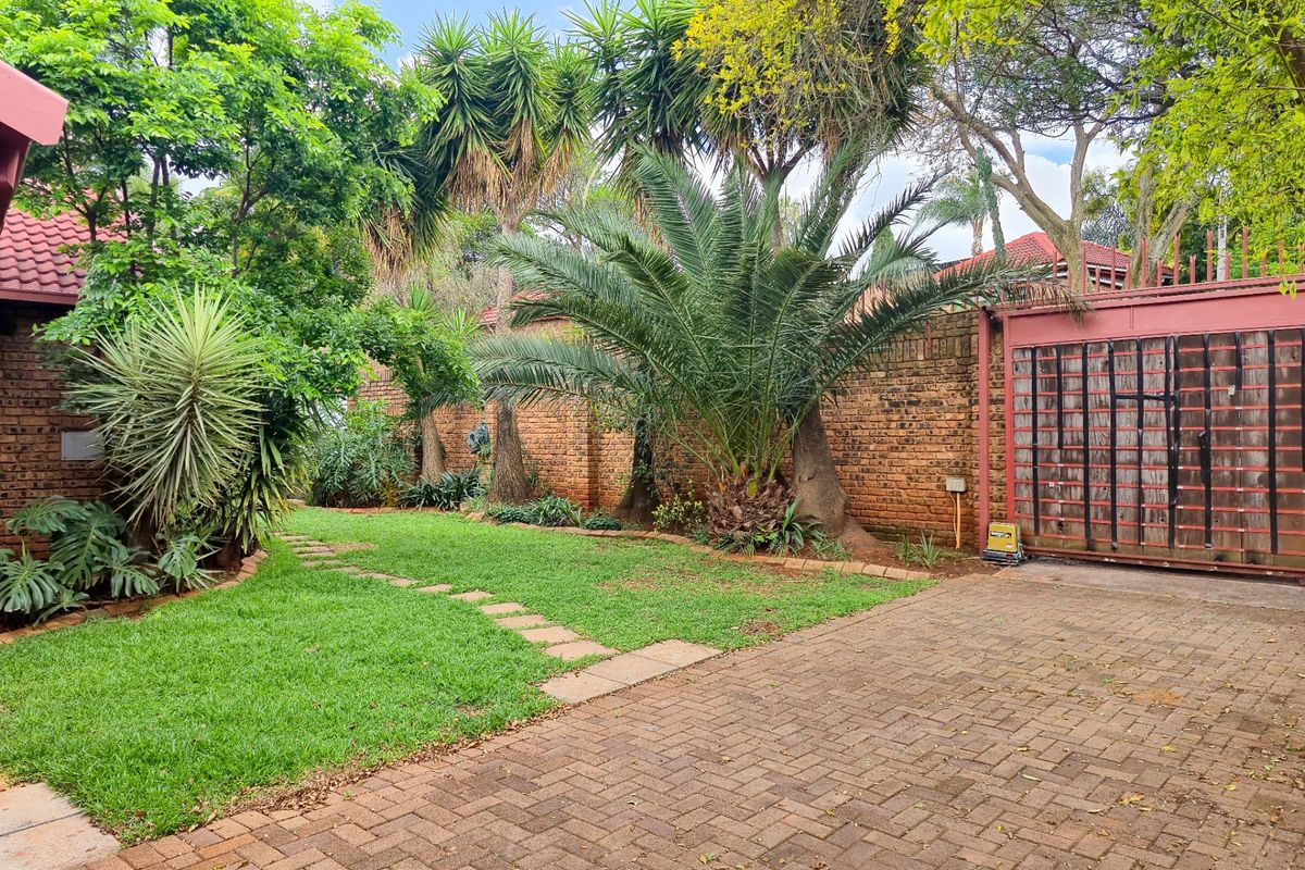 A private rear garden featuring a paved driveway, established trees, a brick boundary wall, and a secure metal sliding gate.
