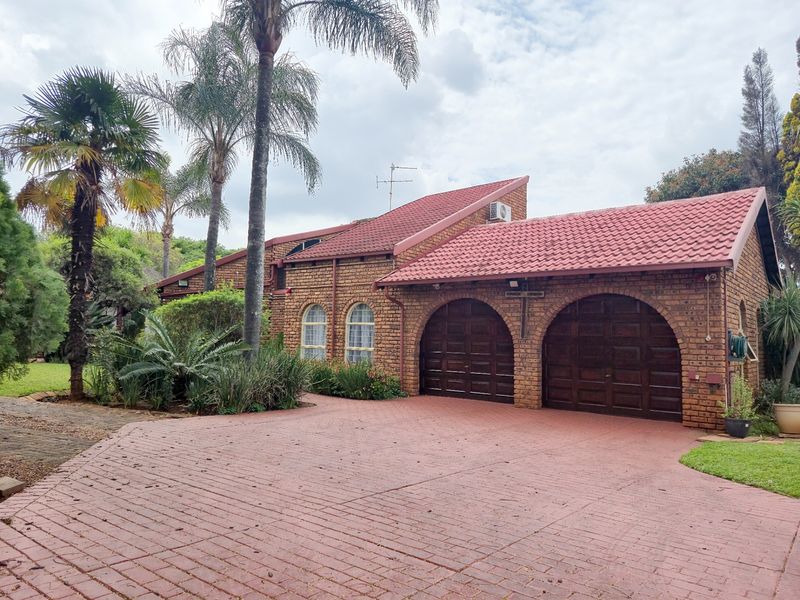 Front elevation of a face-brick house featuring a double arched garage, tiled roof, and a spacious paved driveway surrounded by established garden landscaping.