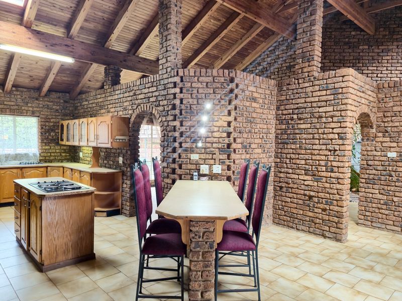 Spacious open-plan kitchen and dining area featuring rustic face brick walls, exposed timber beam ceilings, and a central kitchen island with a built-in hob.