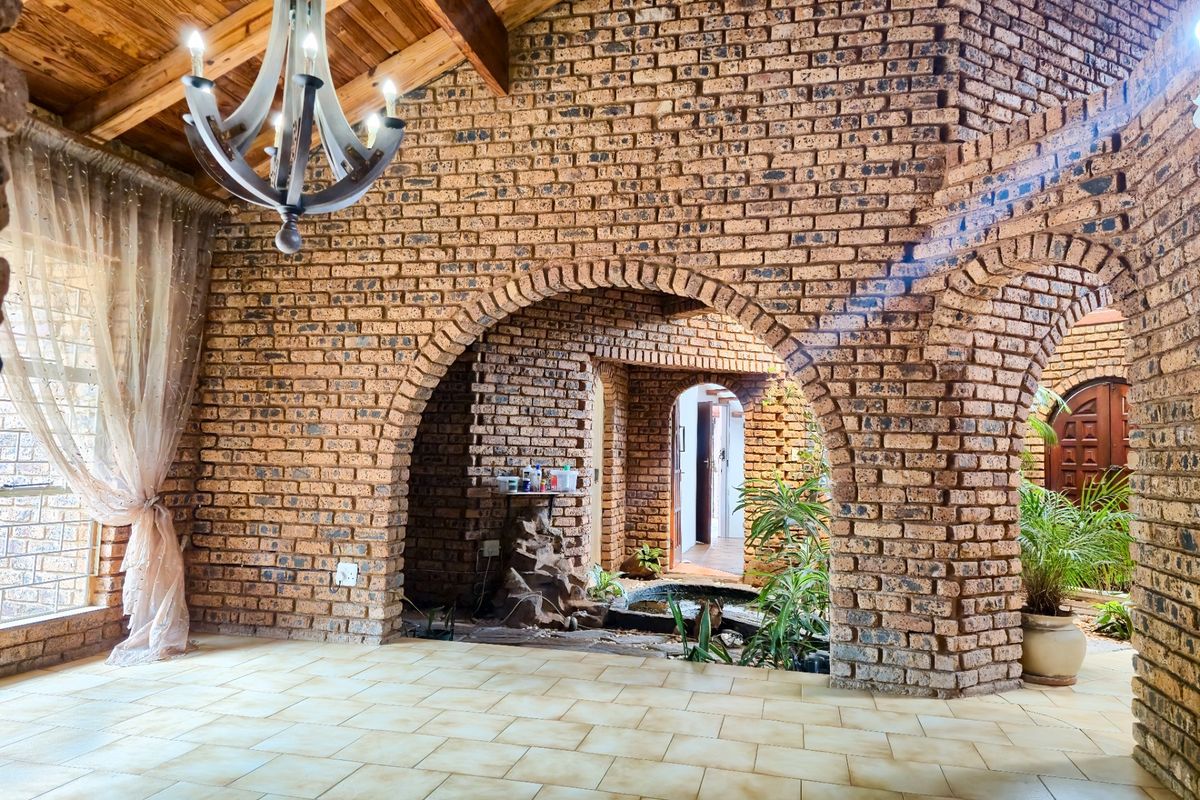Spacious living area featuring rustic exposed brick walls, arched architectural details, a timber beam ceiling, and a unique indoor water feature.