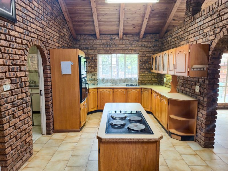 Spacious kitchen featuring exposed brick walls, a timber vaulted ceiling, central island with hob, and ample wooden cabinetry.