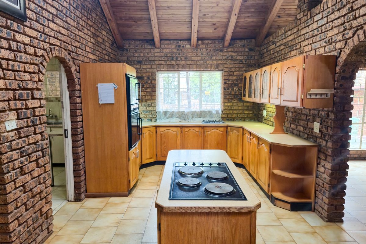 Spacious kitchen featuring exposed brick walls, a timber vaulted ceiling, central island with hob, and ample wooden cabinetry.