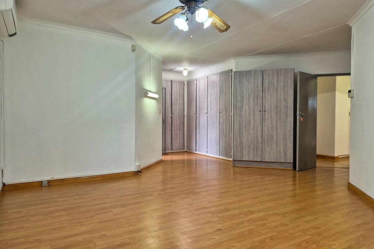 Spacious bedroom featuring laminate flooring, extensive built-in cupboard storage, a ceiling fan, and an integrated air conditioning unit.