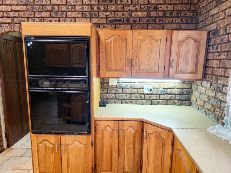 A kitchen area featuring traditional wooden cabinetry, built-in double oven, and rustic exposed brick walls with integrated under-cabinet lighting.