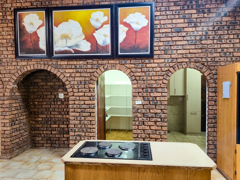 A rustic kitchen featuring exposed brick walls with arched entryways leading to a pantry and utility area, complete with a central island and electric hob.