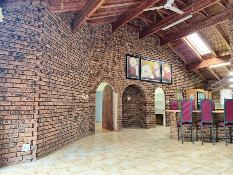 Spacious open-plan living area featuring striking exposed brick walls, high vaulted timber ceilings with exposed trusses, a skylight, and a built-in brick breakfast bar.
