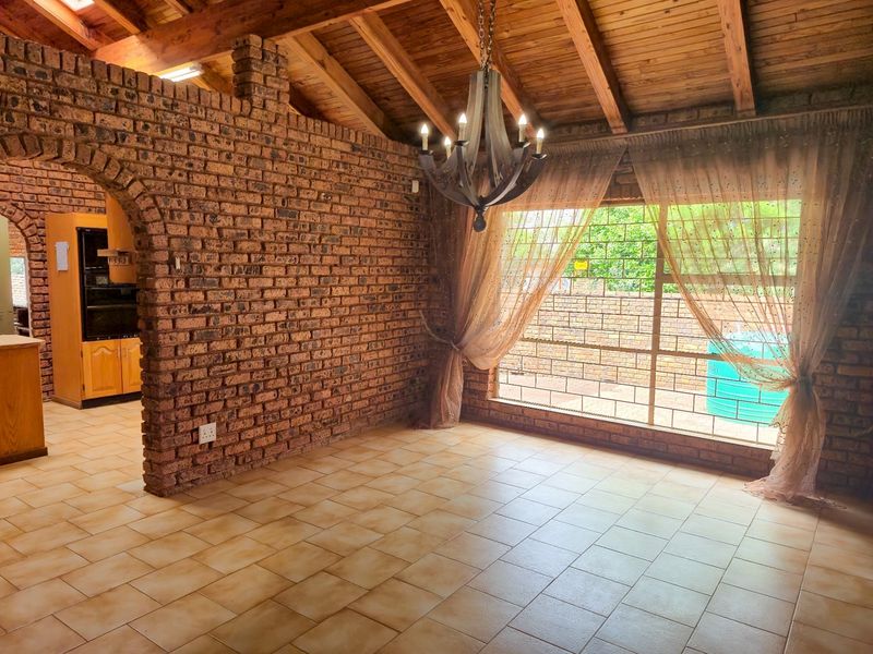 Spacious open-plan living area featuring exposed brick walls, timber beam ceilings, and ceramic floor tiles, with a seamless flow into the adjacent kitchen.