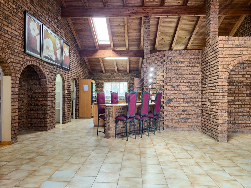 Spacious open-plan living area featuring rustic exposed brick walls, high timber-beamed ceilings with a skylight, and durable ceramic tile flooring.