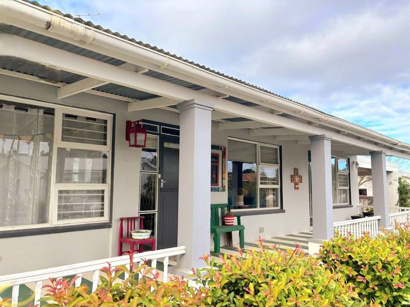 A covered front patio featuring concrete columns, aluminium window frames, and a corrugated metal roof, providing a welcoming entrance to the home.