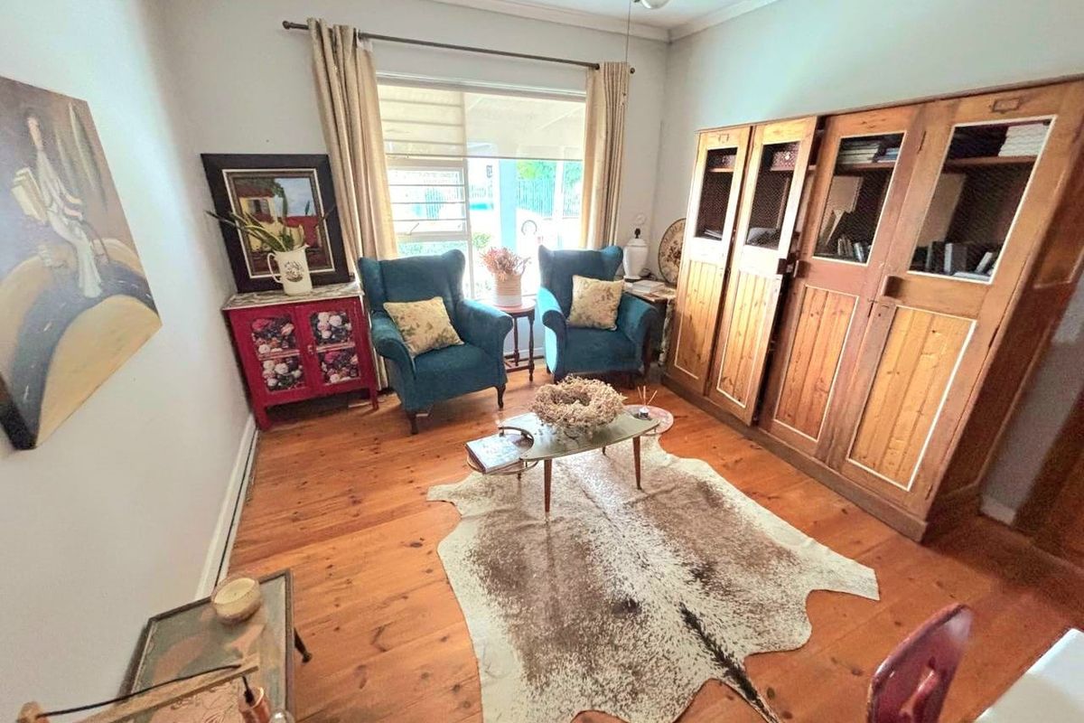 A cozy living room featuring warm timber flooring, a ceiling fan, and natural light through a large window.