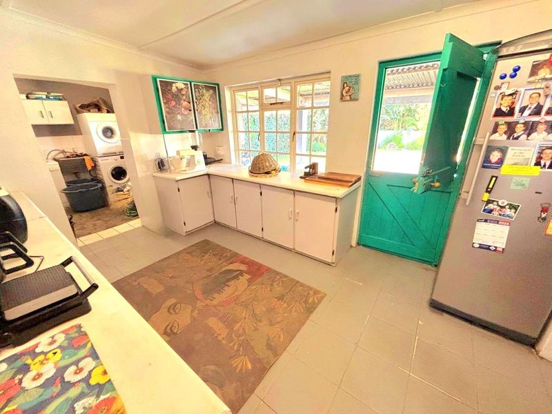 A functional kitchen featuring built-in cabinetry, tiled flooring, and an adjoining scullery area with direct access to the exterior via a stable door.