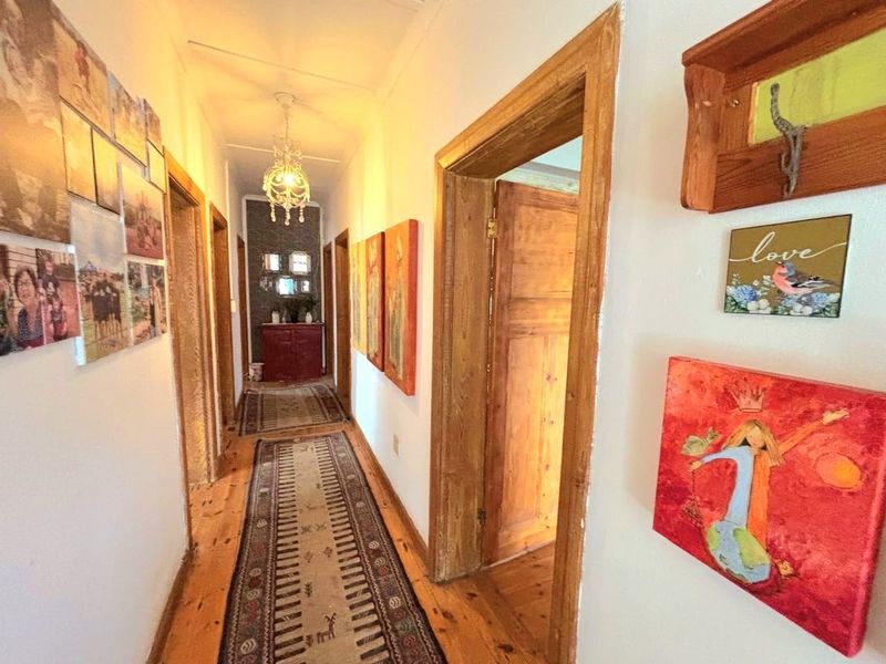 A long hallway featuring warm timber flooring and traditional timber door frames, providing access to multiple rooms within the home.