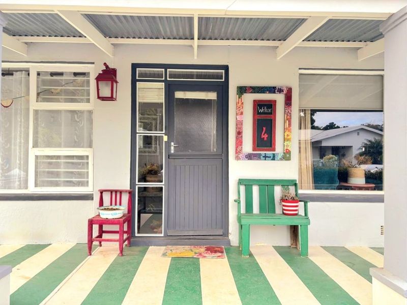 A covered front patio featuring a painted striped concrete floor, a timber-framed entrance door with sidelight, and a wall-mounted light fixture.