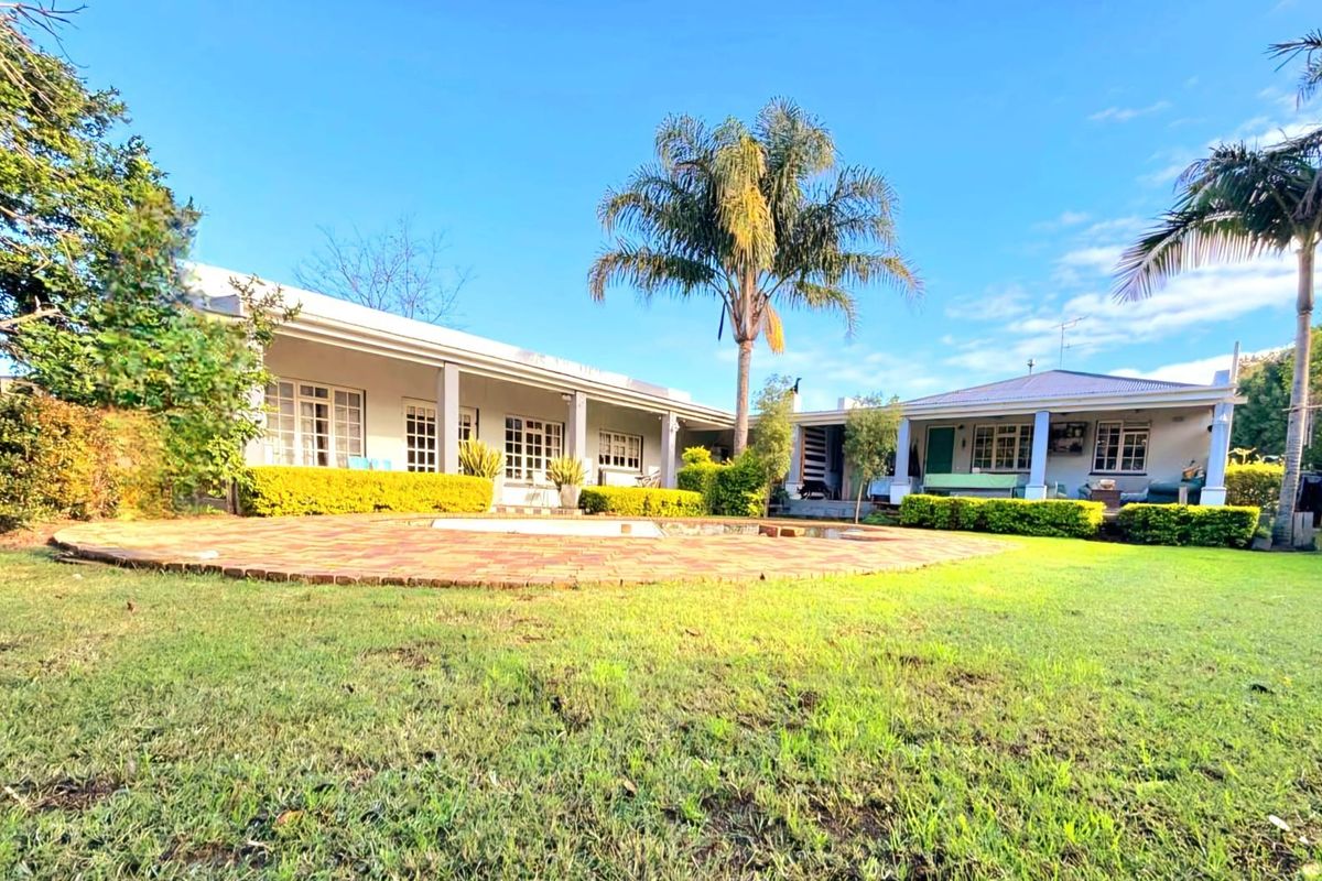 Spacious rear garden featuring a swimming pool with brick paving, a covered patio area, and established landscaping with mature palm trees.