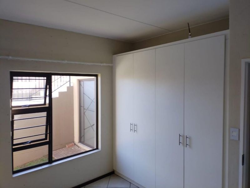 A clean, empty bedroom featuring built-in cupboards, tiled flooring, and an aluminium window with security bars.