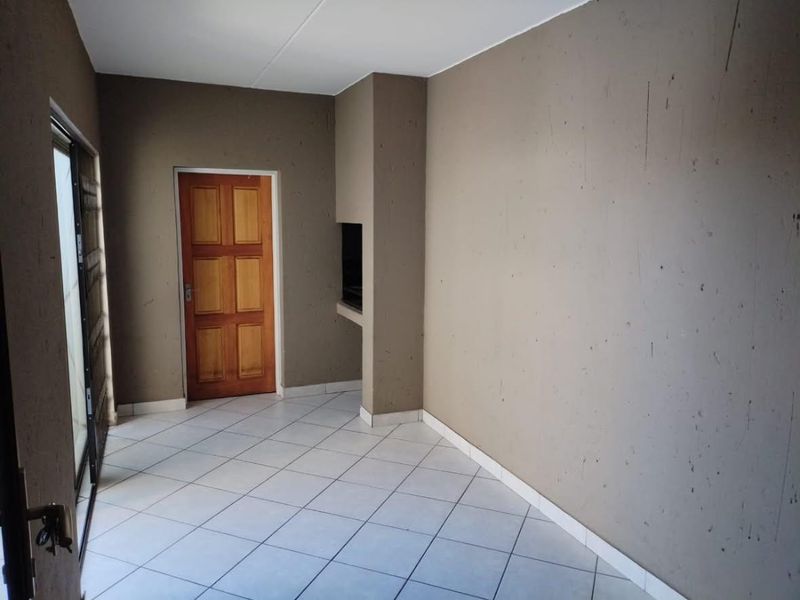 An empty covered patio area featuring tiled flooring, a built-in braai, and access via a sliding door and a wooden door.