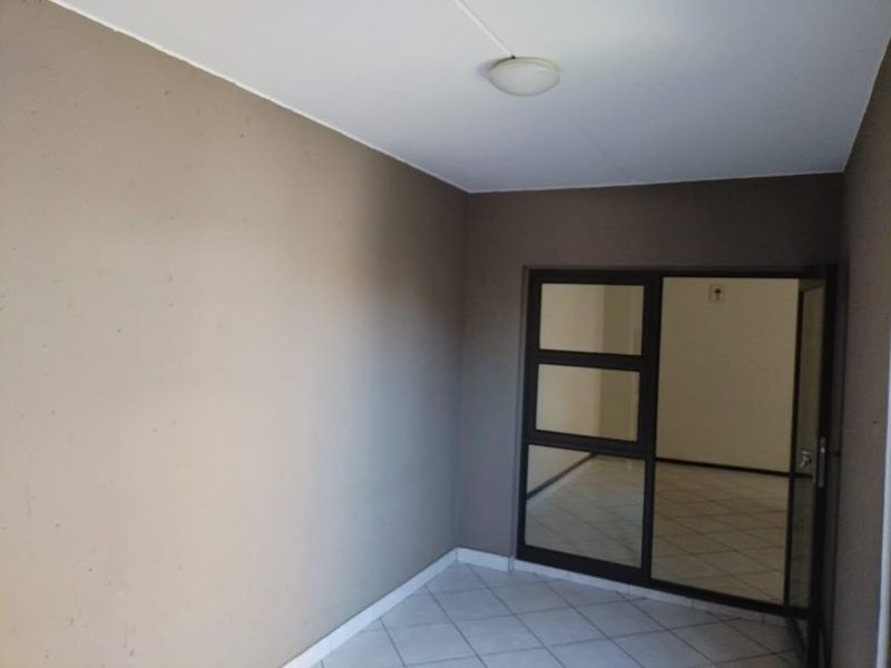 An empty living area featuring neutral wall tones, tiled flooring, and an aluminium framed glass door leading to an adjacent space.