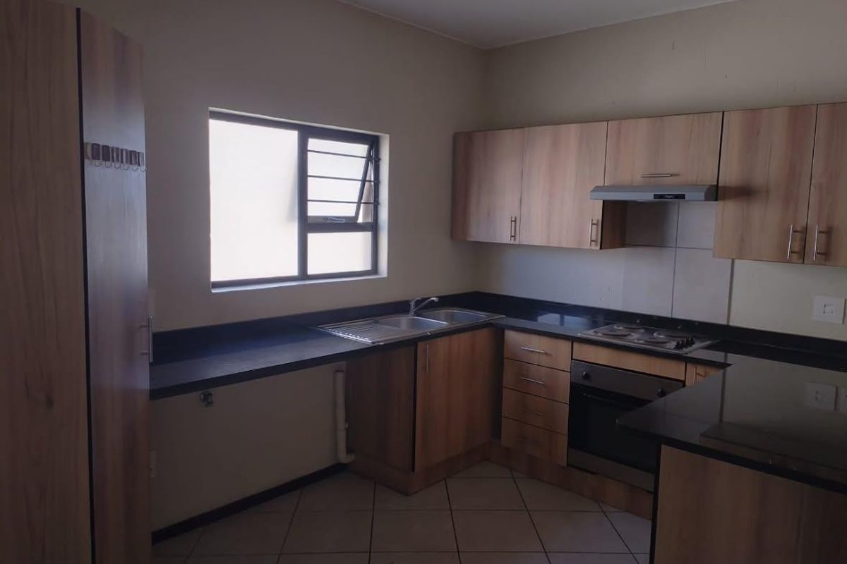 A functional kitchen featuring wood-look cabinetry, black granite countertops, built-in oven, hob, extractor fan, and tiled flooring.