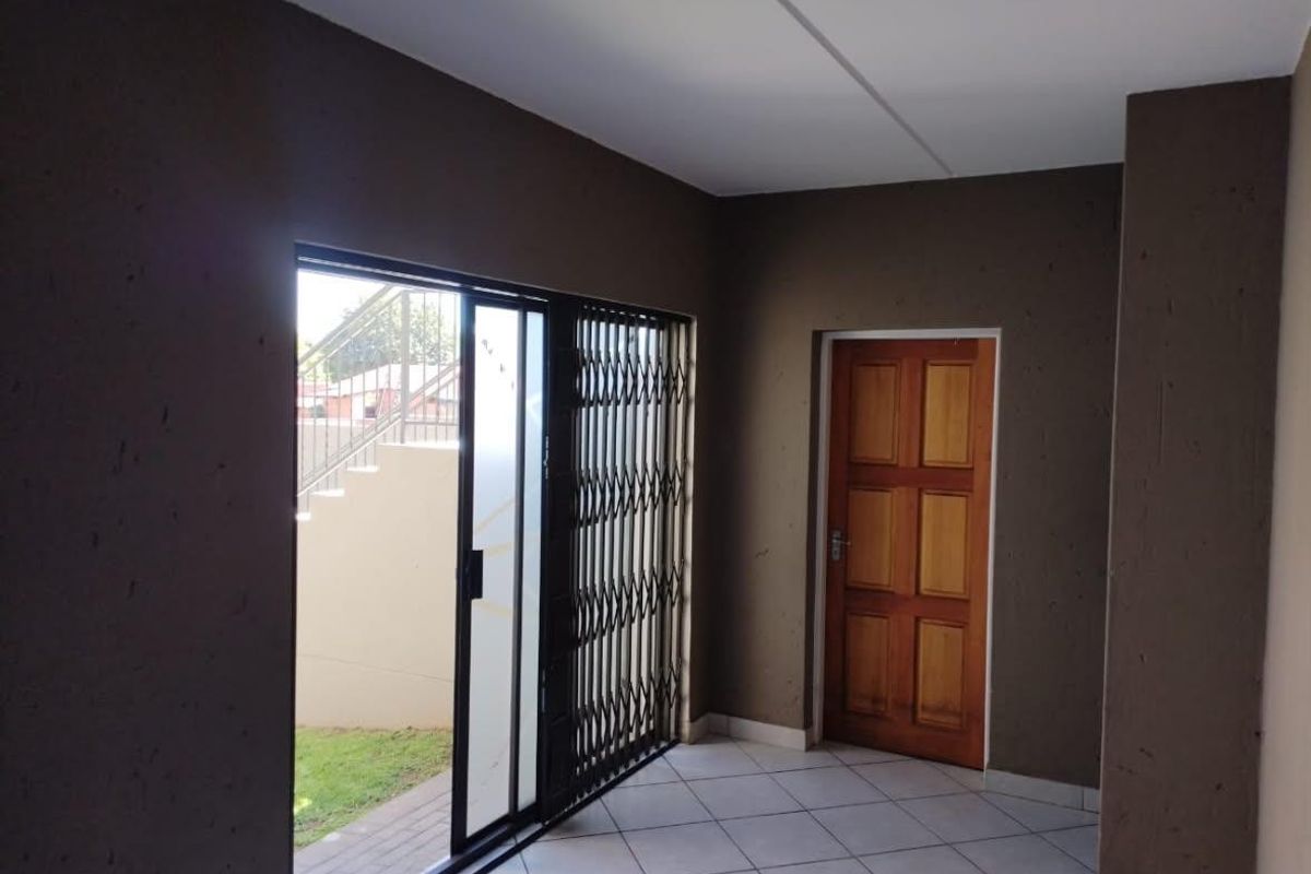 An empty living area featuring tiled flooring, a wooden door, and a sliding glass door with a security gate leading to the exterior.
