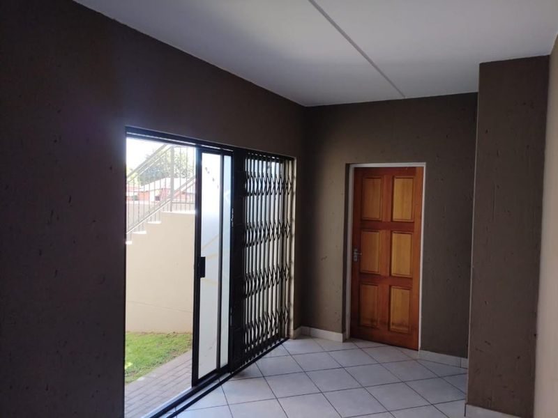 An empty living area featuring tiled flooring, a wooden door, and a sliding glass door with a security gate leading to the exterior.