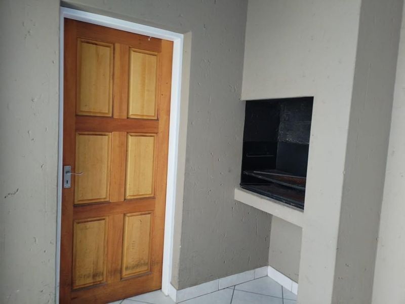 A covered patio area featuring a built-in braai, tiled flooring, and a wooden entrance door.