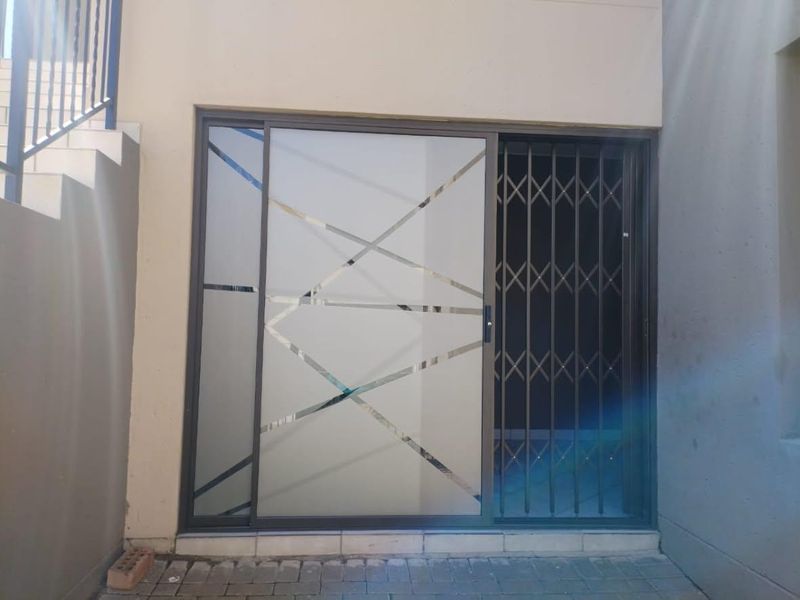 A secure patio entrance featuring a modern sliding glass door with geometric frosted detailing and a sturdy metal security gate.