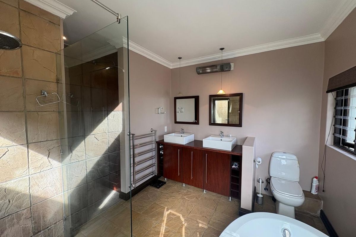 Spacious bathroom featuring a double vanity with vessel sinks, a large walk-in shower with stone cladding, a freestanding bathtub, and a heated towel rail.