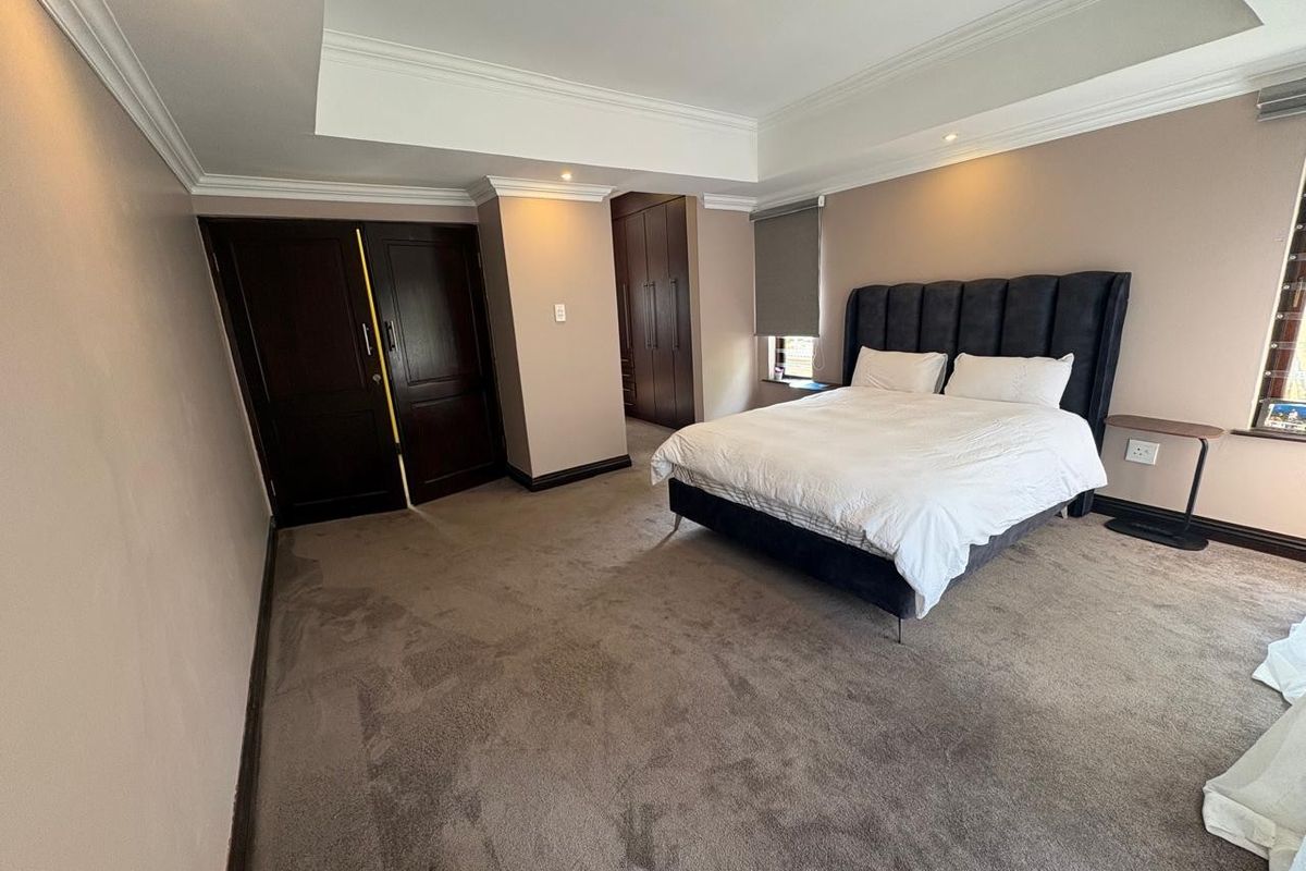 Spacious bedroom featuring neutral walls, plush carpeting, recessed ceiling with downlights, and ample built-in cupboard storage.