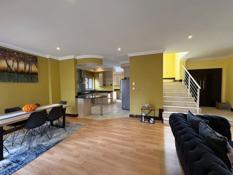 Spacious open-plan living and dining area featuring a modern kitchen with granite countertops, laminate flooring, and a staircase leading to the upper level.