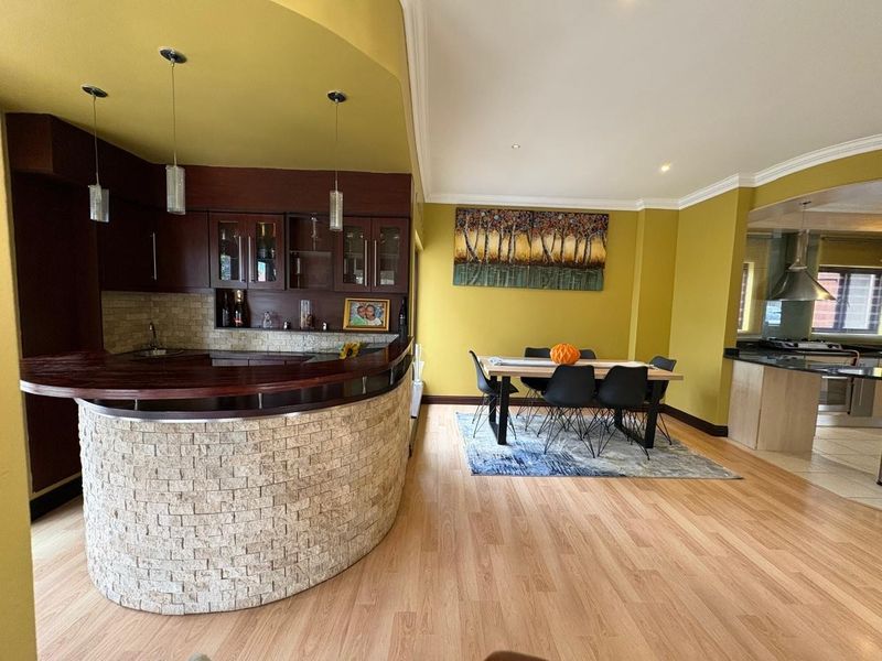 Open-plan living area featuring a distinctive curved stone-clad breakfast bar, dark wood cabinetry, and a dedicated dining space with laminate flooring throughout.