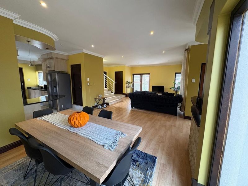 Spacious open-plan living and dining area featuring laminate flooring, recessed lighting, and a modern staircase, seamlessly connected to the kitchen.