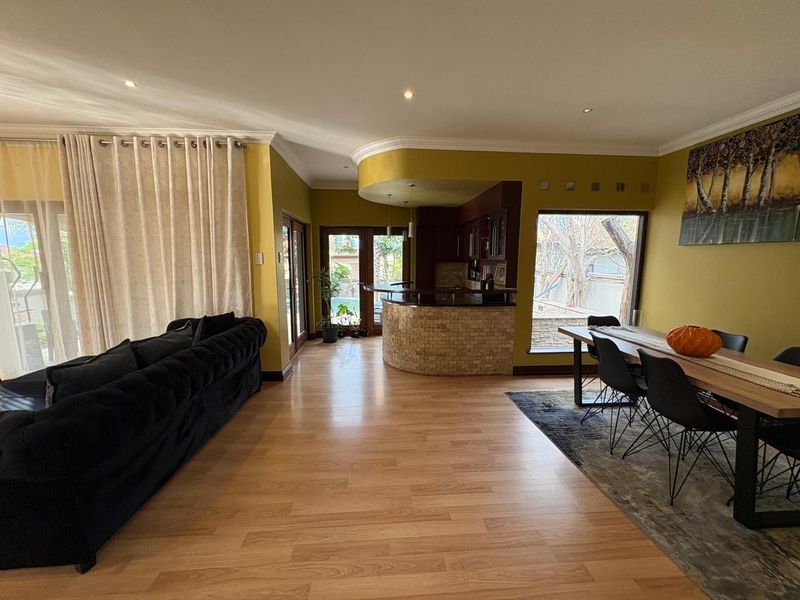 Spacious open-plan living and dining area featuring laminate flooring, recessed lighting, and a stone-clad breakfast bar connecting to the kitchen.