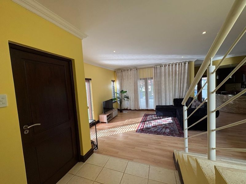 Spacious open-plan living area featuring laminate flooring, a feature staircase, and sliding glass doors that provide ample natural light.