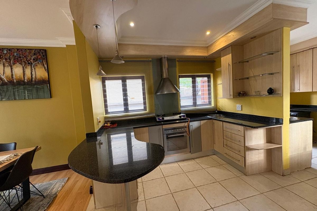 A functional kitchen featuring granite countertops, a breakfast bar, built-in oven, extractor fan, and tiled flooring with ample cabinetry.