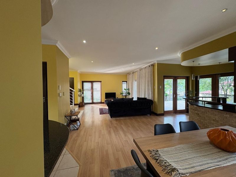Spacious open-plan living and dining area featuring laminate flooring, recessed lighting, and a stone-clad breakfast bar with direct access to the patio.