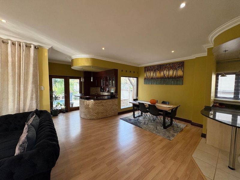 Spacious open-plan living and dining area featuring a built-in bar with stone cladding, laminate flooring, and recessed lighting, offering a functional entertainment space.